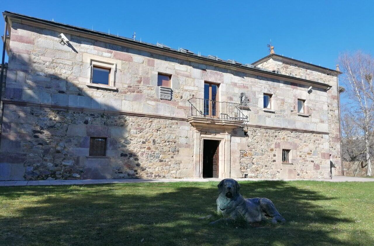 Fachada de la Casa del Parque de Babia con un perro de piedra en el césped