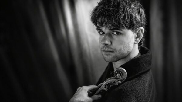 Violinista Stefan Estrada posando con su violín en un fondo oscuro