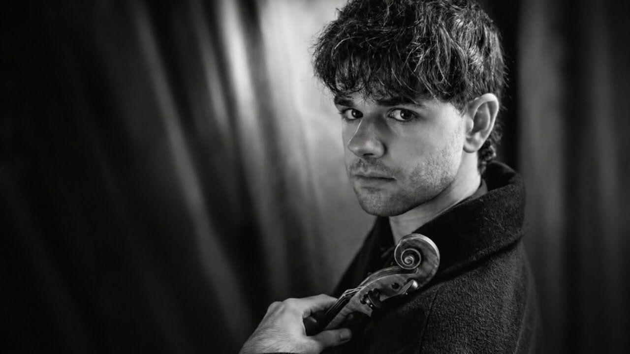 Violinista Stefan Estrada posando con su violín en un fondo oscuro