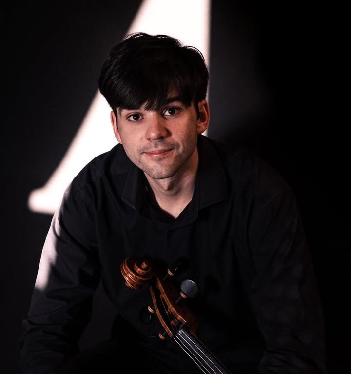 Músico posando con un violonchelo en un fondo oscuro