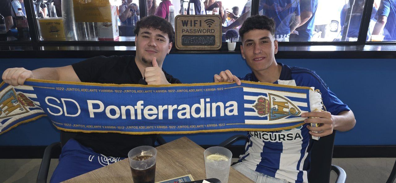 Dos jóvenes mostrando una bufanda de la SD Ponferradina en un bar