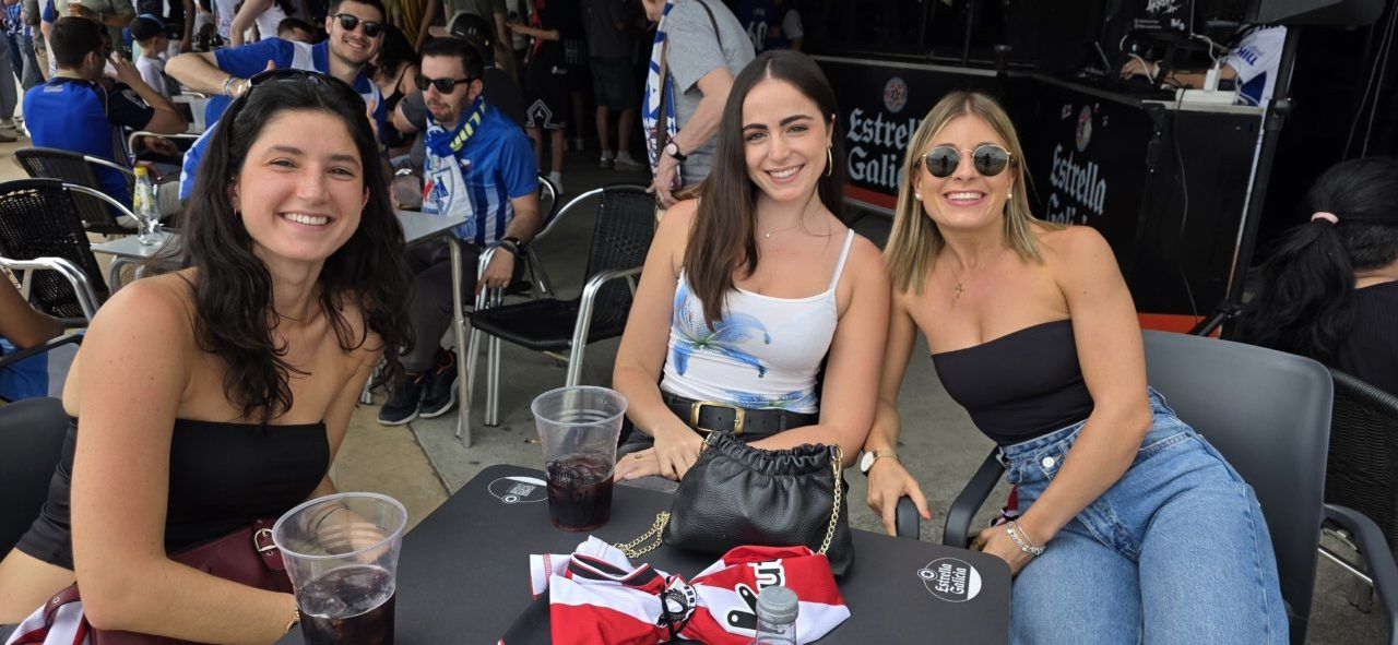 Tres mujeres sonriendo en un bar durante un evento deportivo.