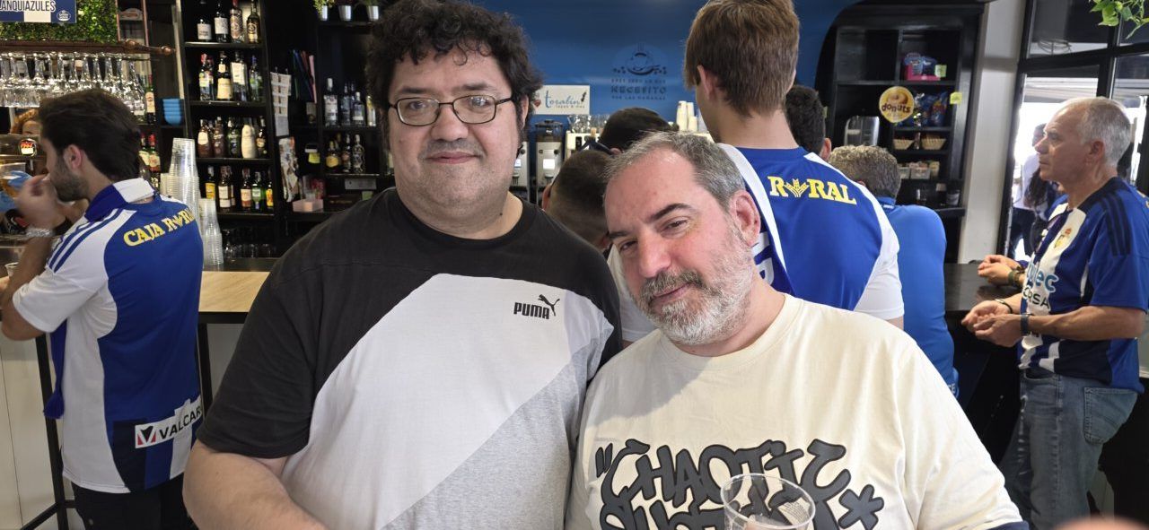 Dos hombres sonriendo en el Bar El Toralín con aficionados de la Ponfe detrás.