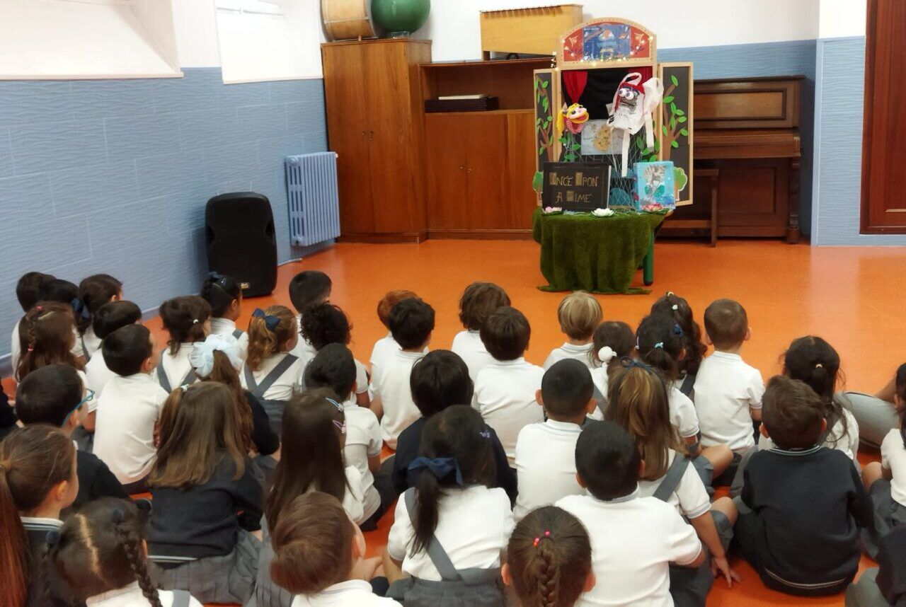 Niños sentados frente a un teatro de marionetas en un taller escolar