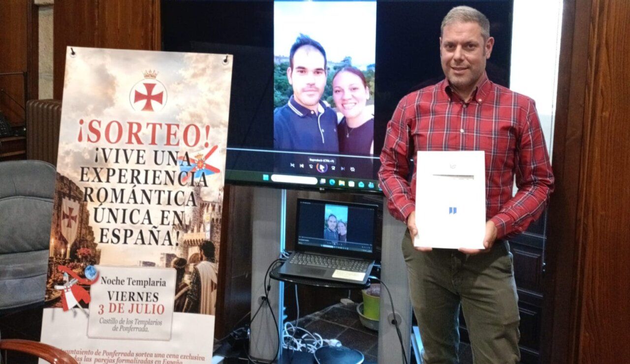 Hombre sosteniendo un premio frente a una pantalla con una pareja