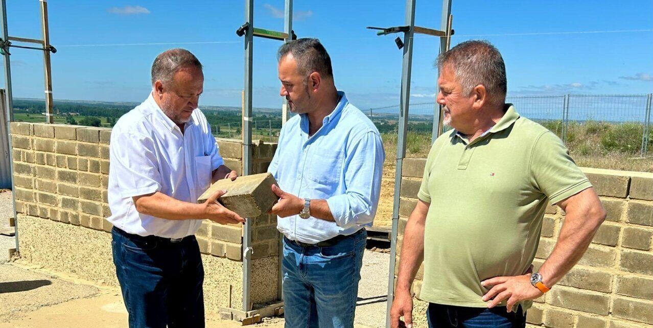 Visita a las obras del Centro Arqueológico de Lancia con tres hombres observando un bloque de construcción.