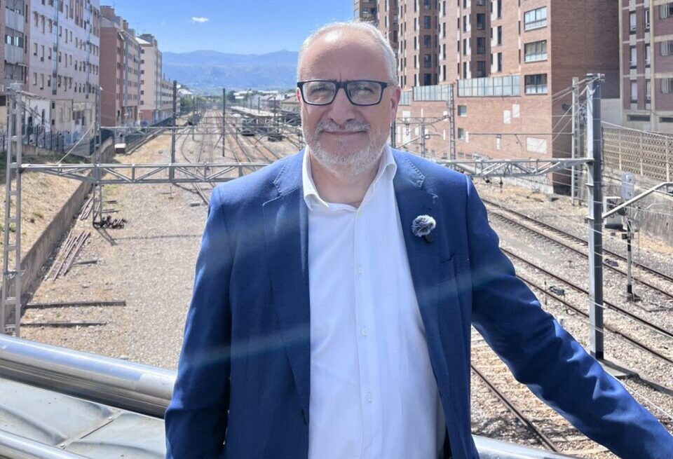 Hombre con traje frente a vías de tren y edificios