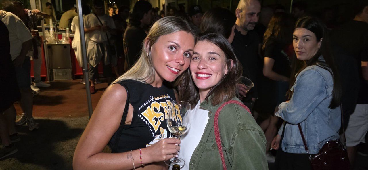 Dos mujeres sonriendo en un festival con copas en mano