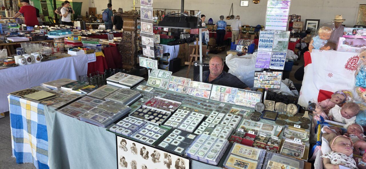 Puesto de antigüedades con monedas, libros y muñecas en feria