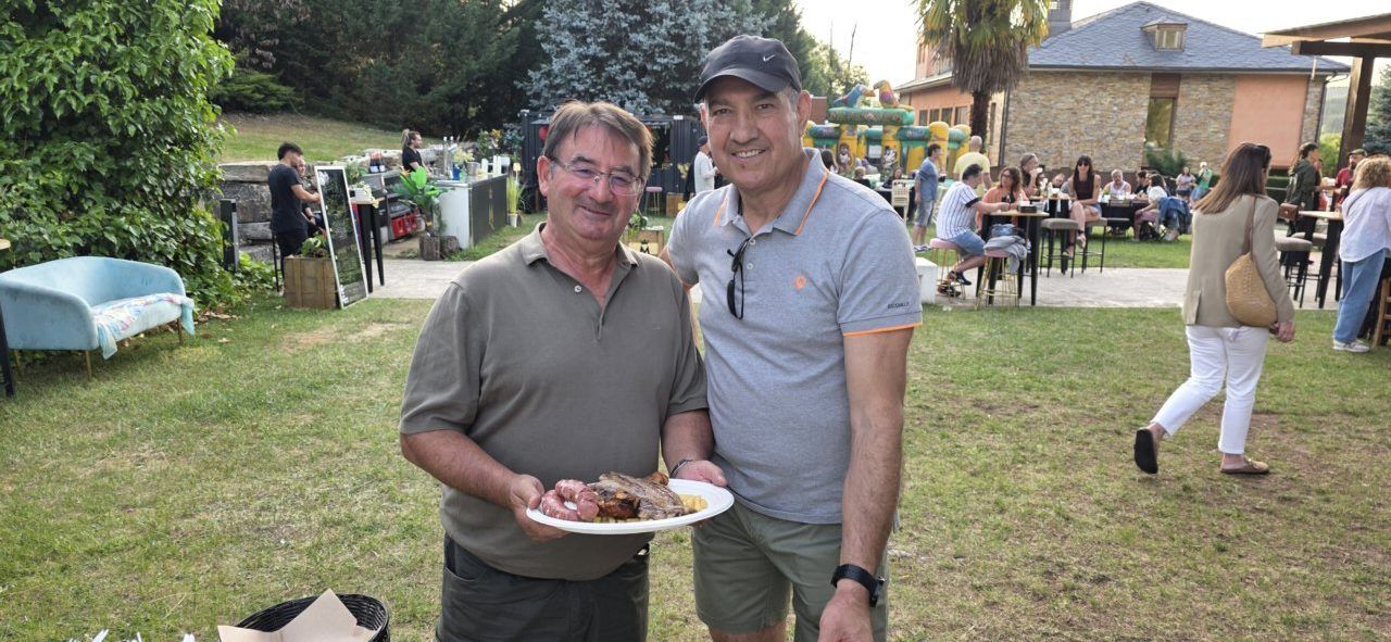 Dos hombres sonrientes sosteniendo un plato de comida en la inauguración de la terraza de verano.