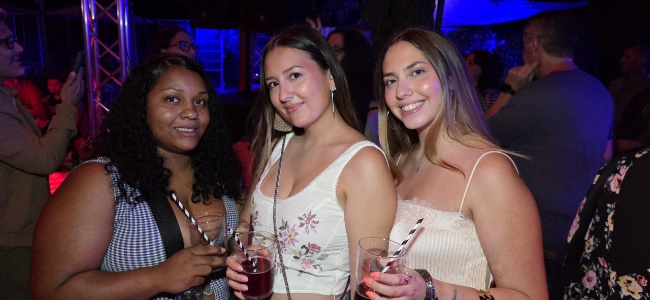 Tres mujeres sonrientes sosteniendo bebidas en un evento social