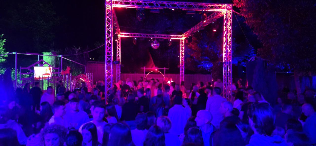 Fiesta nocturna en Vega de Espinareda con luces de colores y gente bailando.