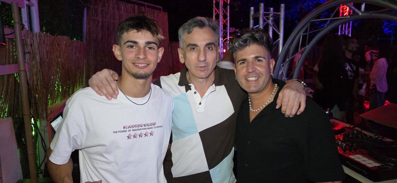 Tres hombres sonriendo en una fiesta con luces de fondo