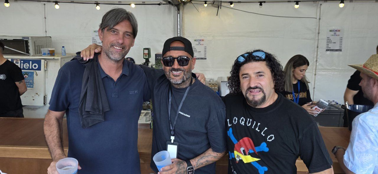 Tres hombres sonriendo en un festival de música con bebidas en la mano.