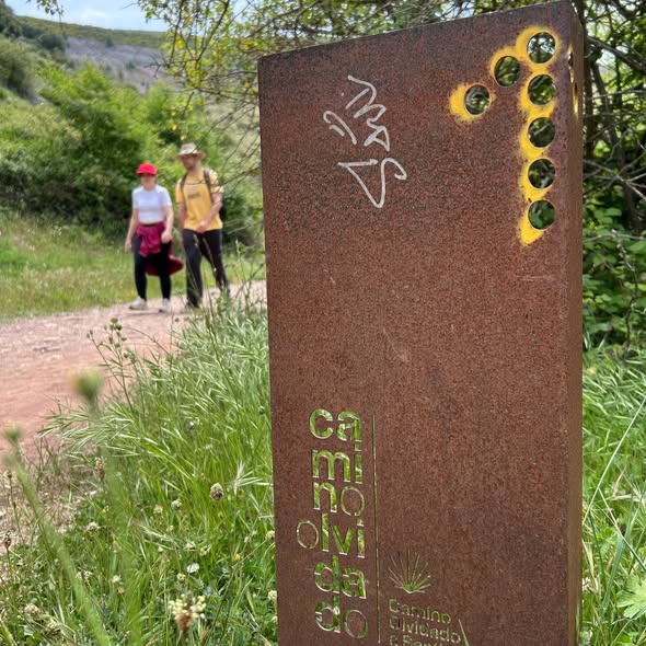 Señal del Camino Olvidado con senderistas en el fondo