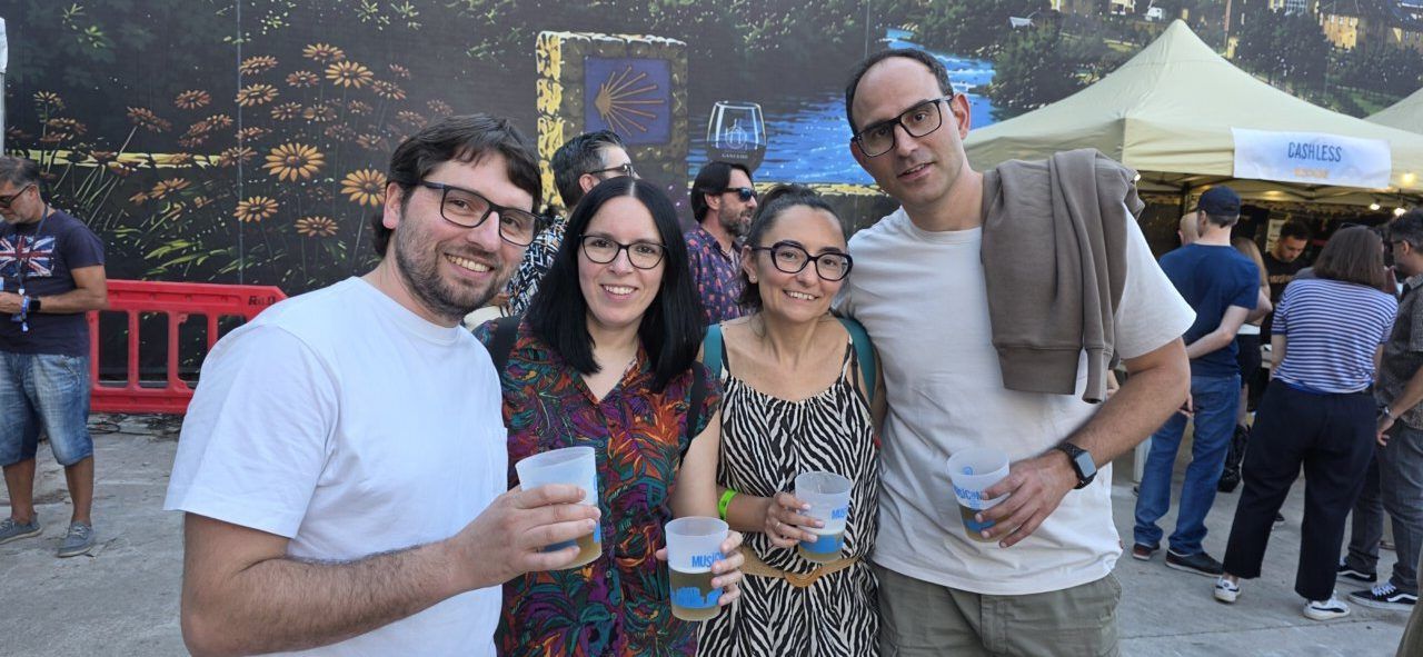 Cuatro personas sonrientes sosteniendo vasos en un evento al aire libre