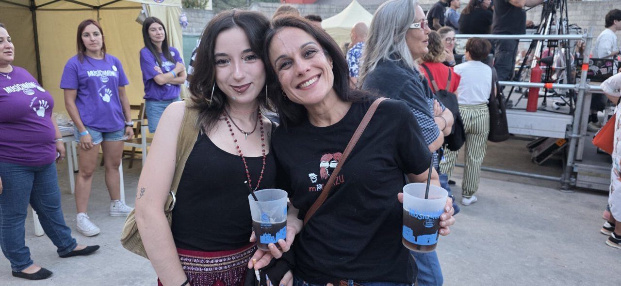Dos mujeres sonrientes en un evento musical con vasos en la mano