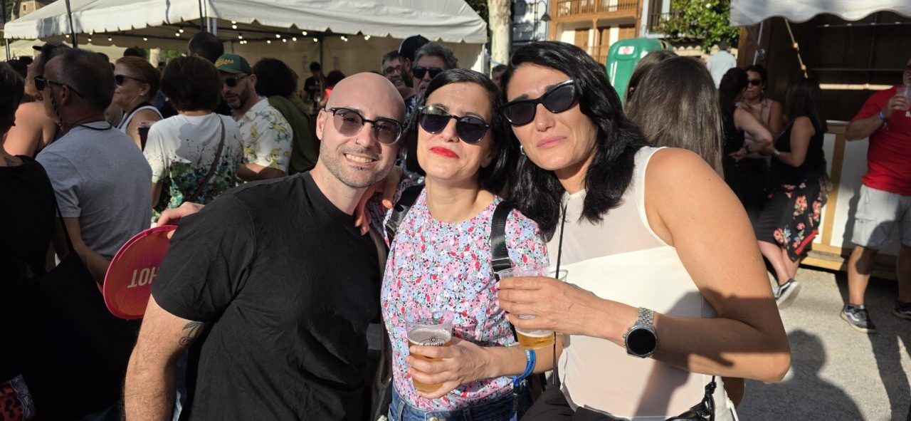 Tres personas sonrientes en un evento al aire libre con bebidas.