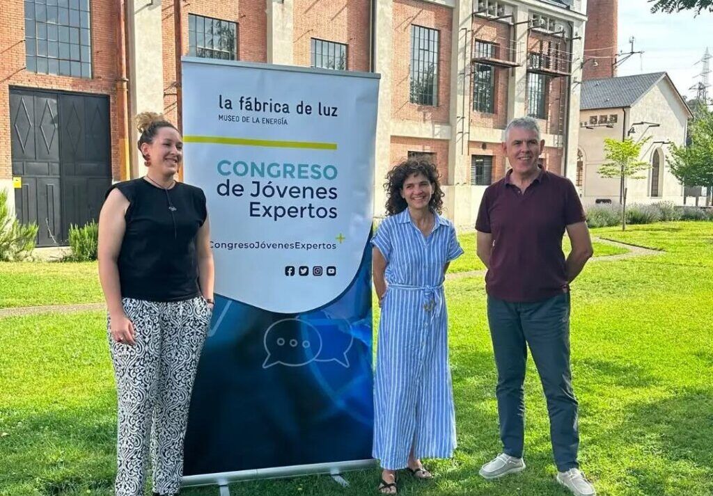 Tres personas posando frente a un cartel del congreso de jóvenes expertos