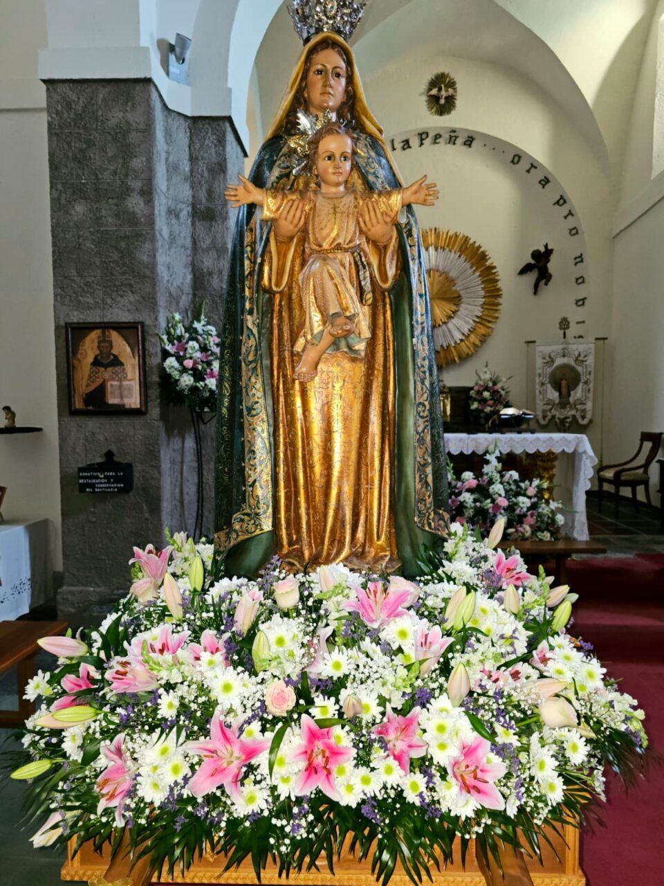 Estatua de la Virgen de la Peña con flores en el altar