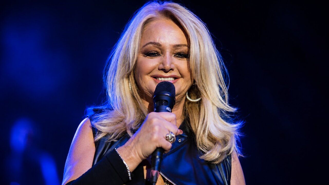Bonnie Tyler sonriendo mientras sostiene un micrófono en un escenario