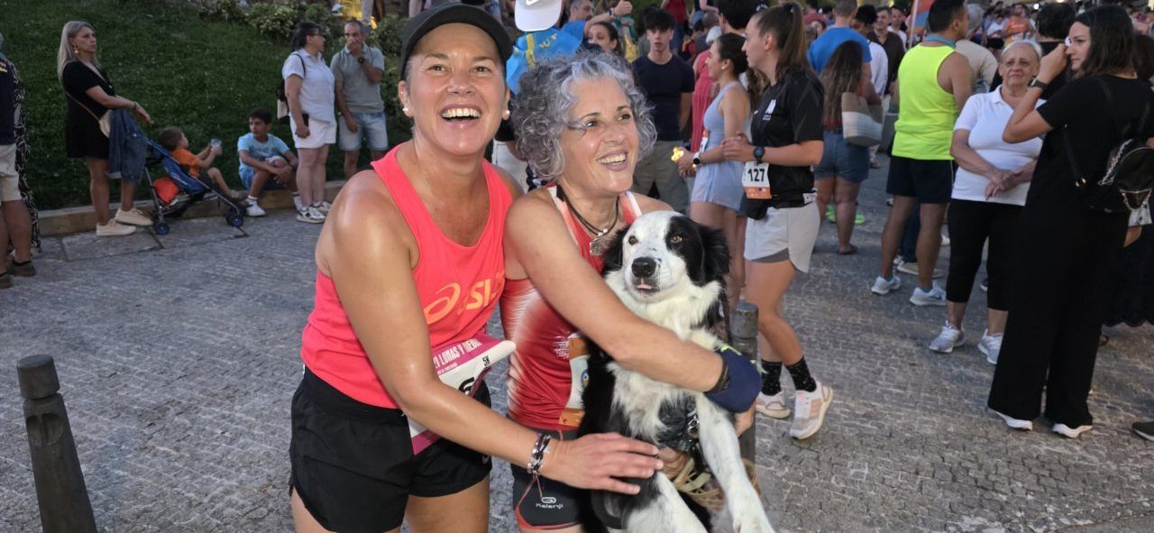 Dos mujeres sonrientes abrazando a un perro en una carrera nocturna