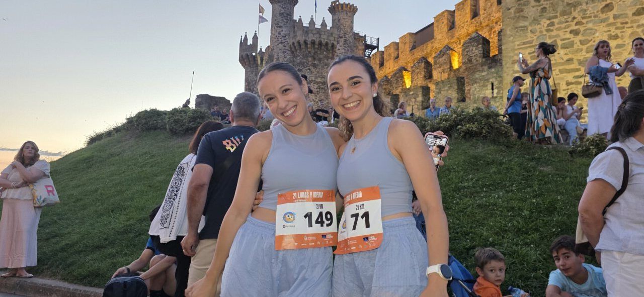 Dos corredoras sonrientes con números en la carrera nocturna en Ponferrada.