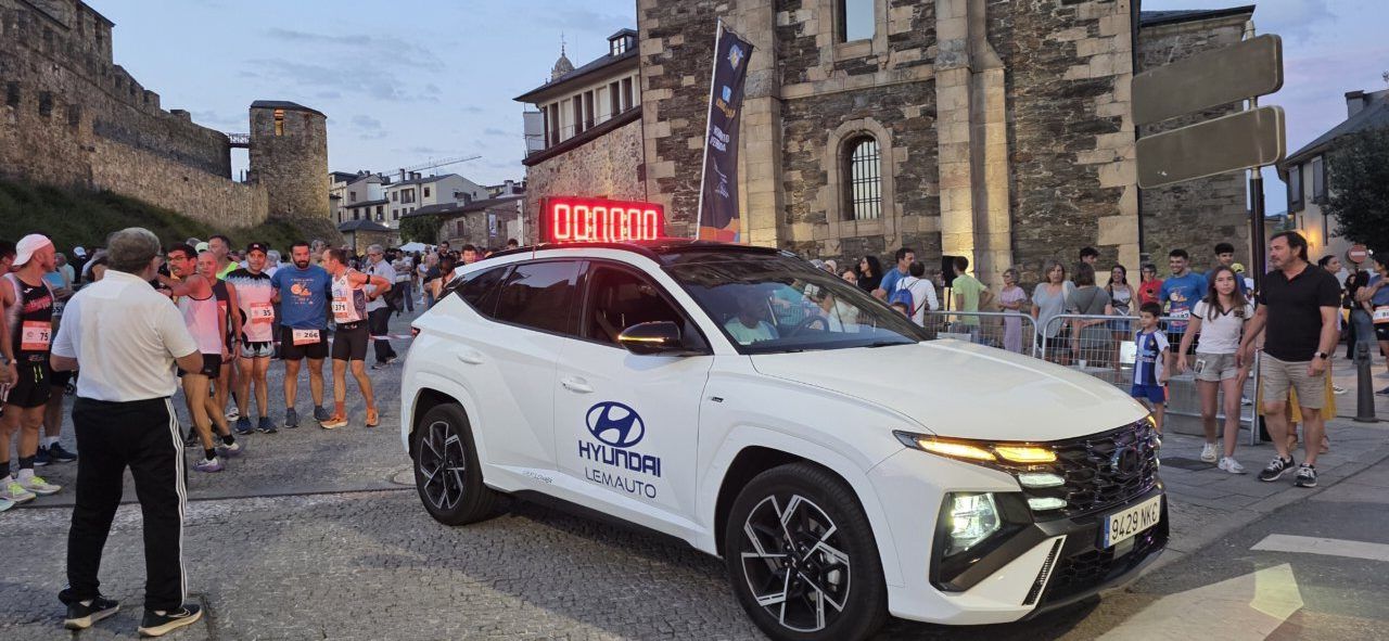Corredores listos para la carrera nocturna en Ponferrada junto a un coche de apoyo.