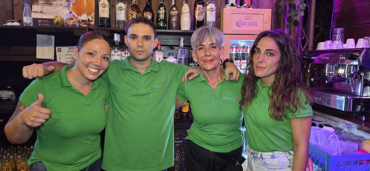 Cuatro personas sonriendo en un bar con camisetas verdes