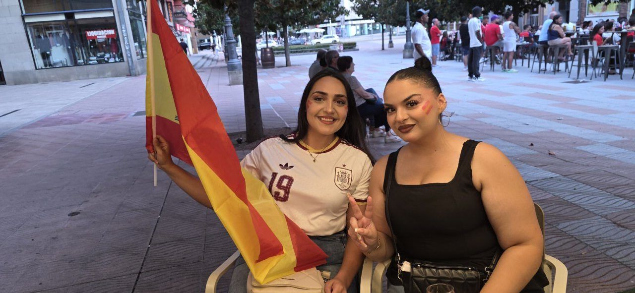 Dos mujeres sonrientes con la bandera de España en un bar de Ponferrada