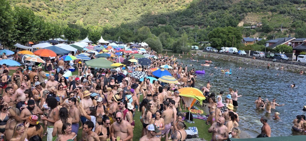 Multitud de personas disfrutando en un festival al aire libre junto a un río.