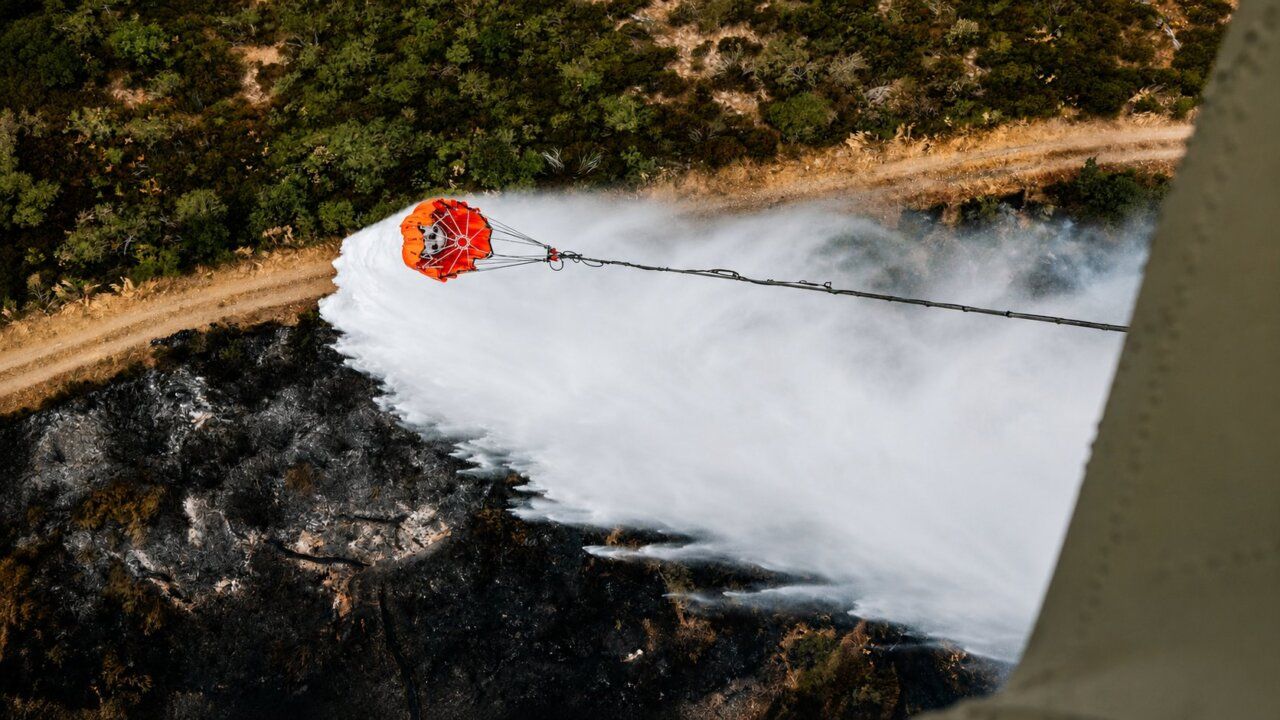Helicóptero lanzando agua sobre un incendio forestal en la zona afectada