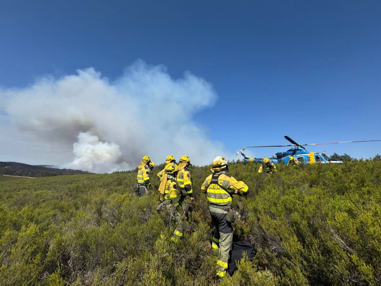 Bomberos trabajando en el incendio de Espina de Tremor con un helicóptero en el fondo.