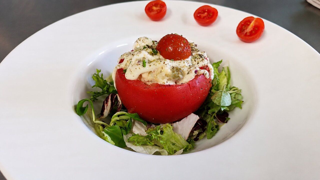 Tomate relleno de ensaladilla sobre una cama de lechuga fresca