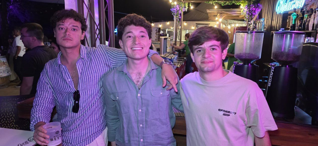 Tres jóvenes sonriendo en un bar iluminado con luces de colores