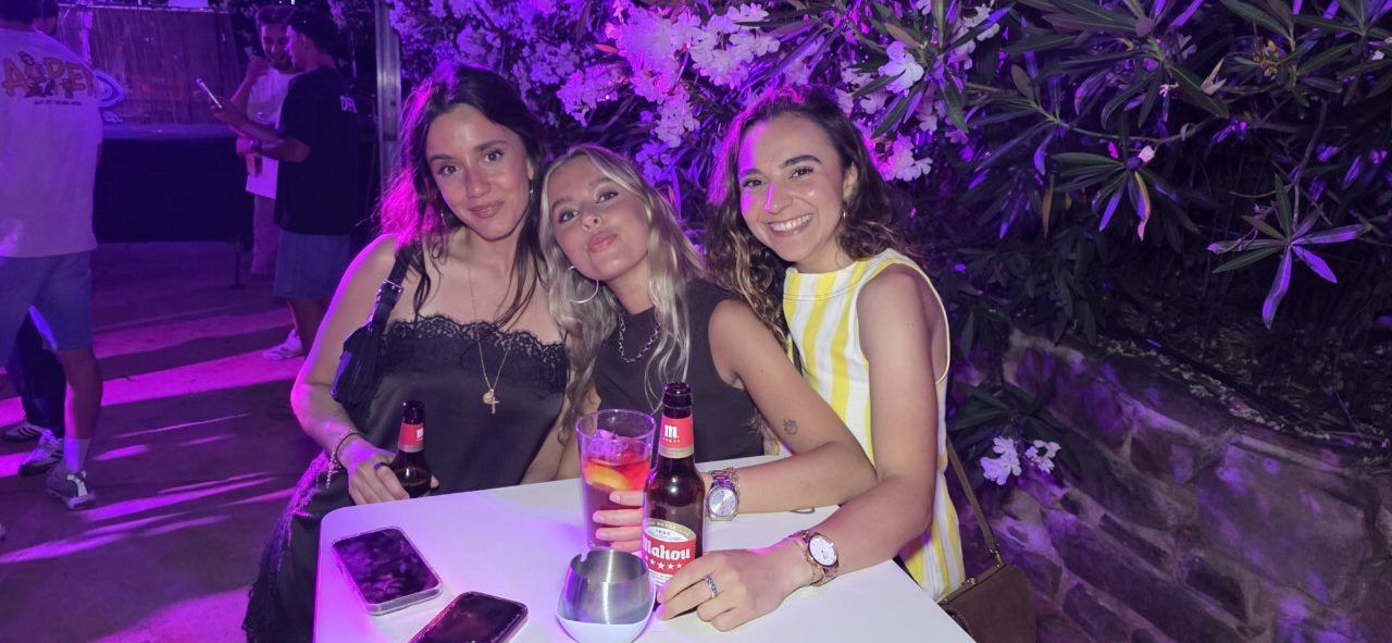 Tres mujeres sonrientes en una fiesta nocturna con bebidas