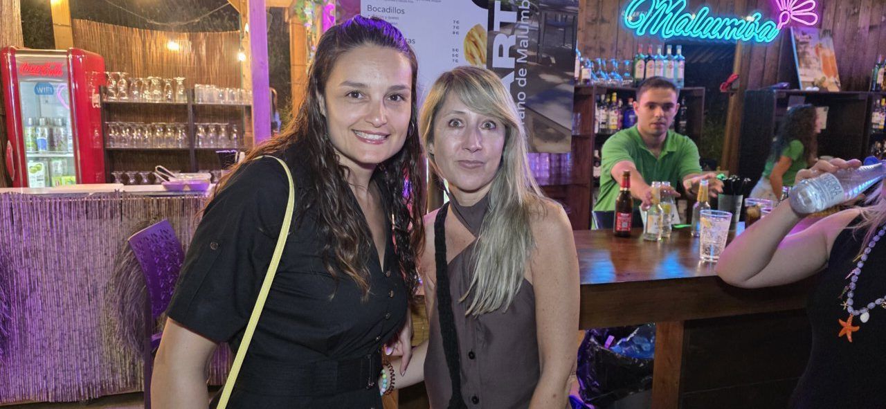 Dos mujeres sonriendo en un bar con luces de colores