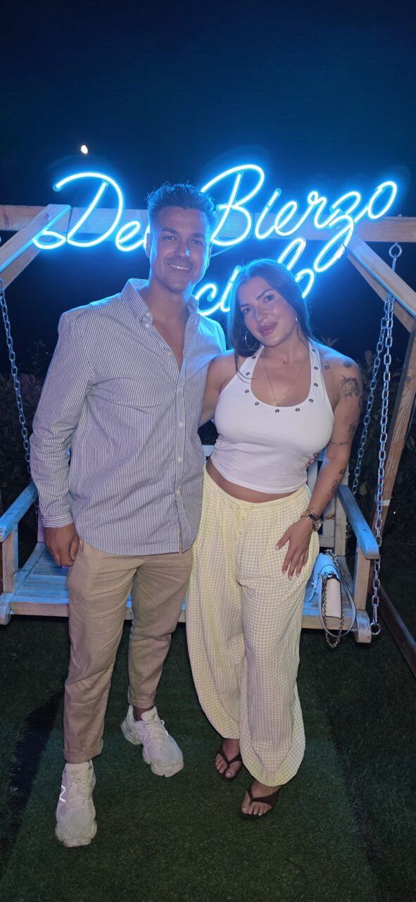 Pareja posando frente a un letrero luminoso en la noche