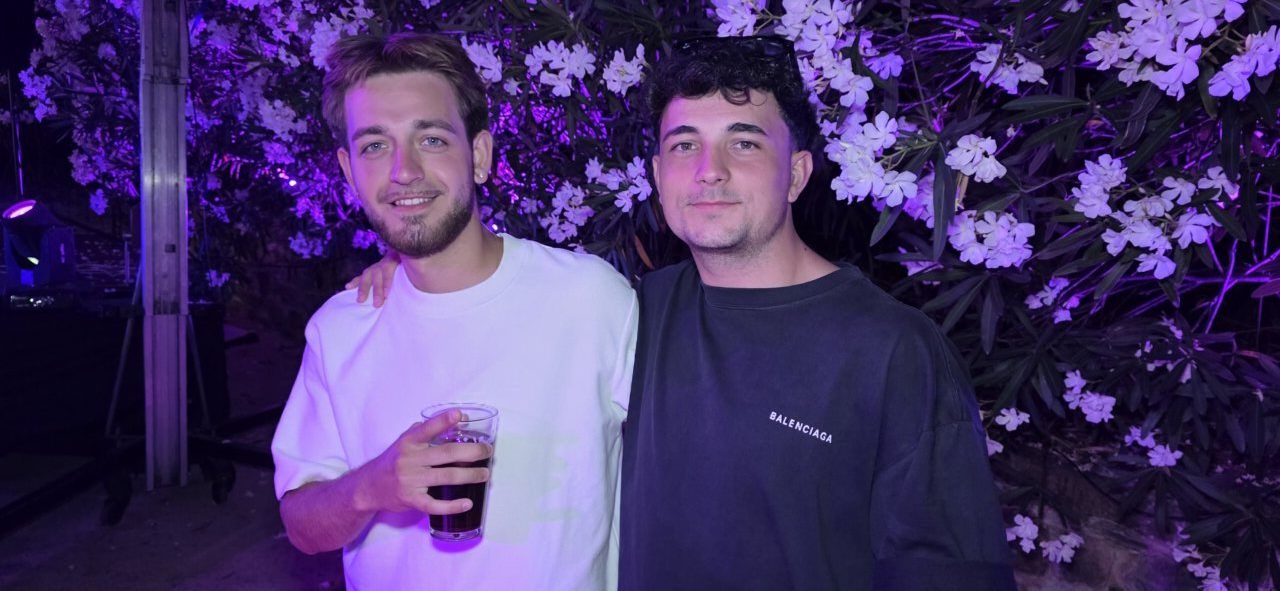 Dos amigos sonriendo en una fiesta con flores de fondo