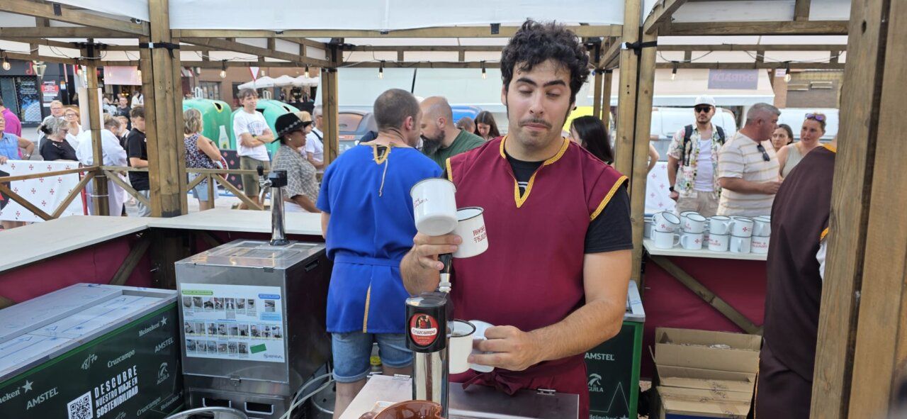 Vendedor en mercado medieval sirviendo bebidas a los visitantes.