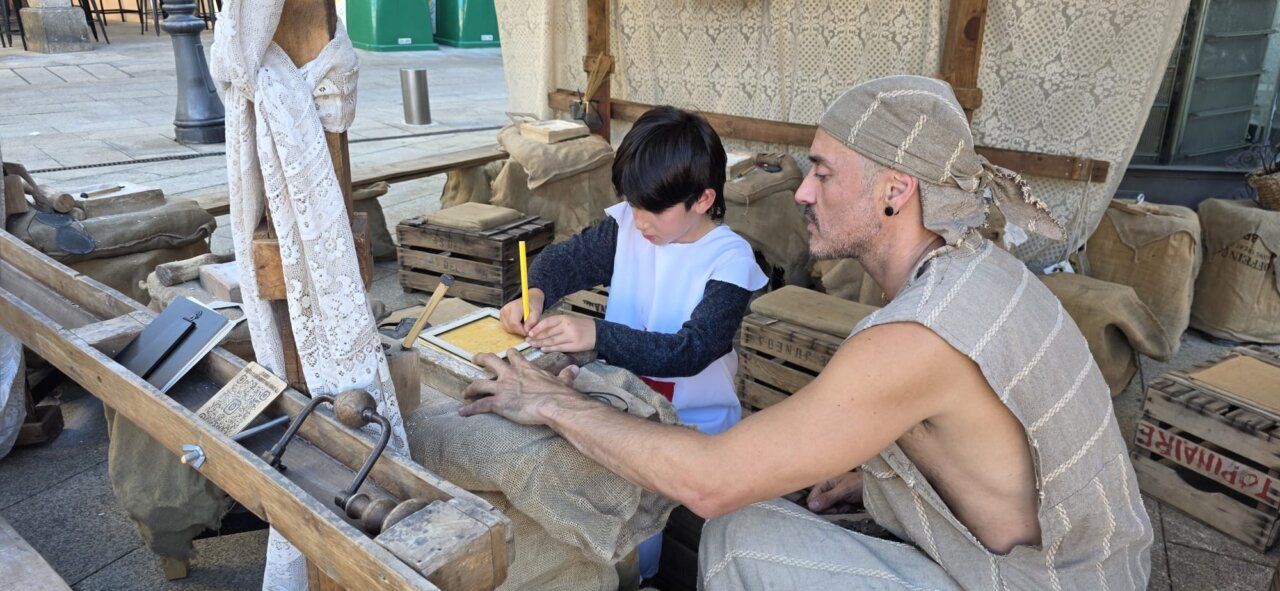 Un niño y un adulto en un mercado medieval, trabajando juntos en un proyecto.