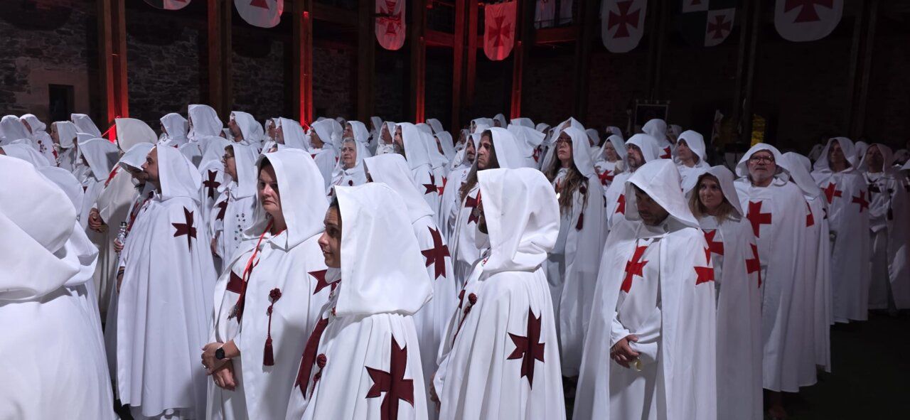 Ceremonia de ordenación templaria con participantes en capas blancas y cruces rojas.