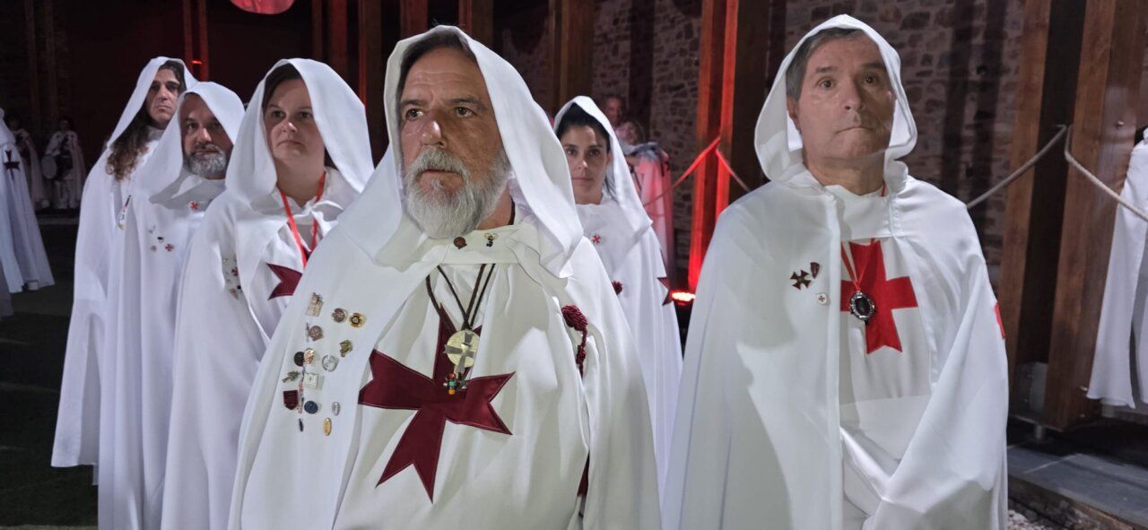 Grupo de personas con túnicas blancas y cruces rojas en ceremonia