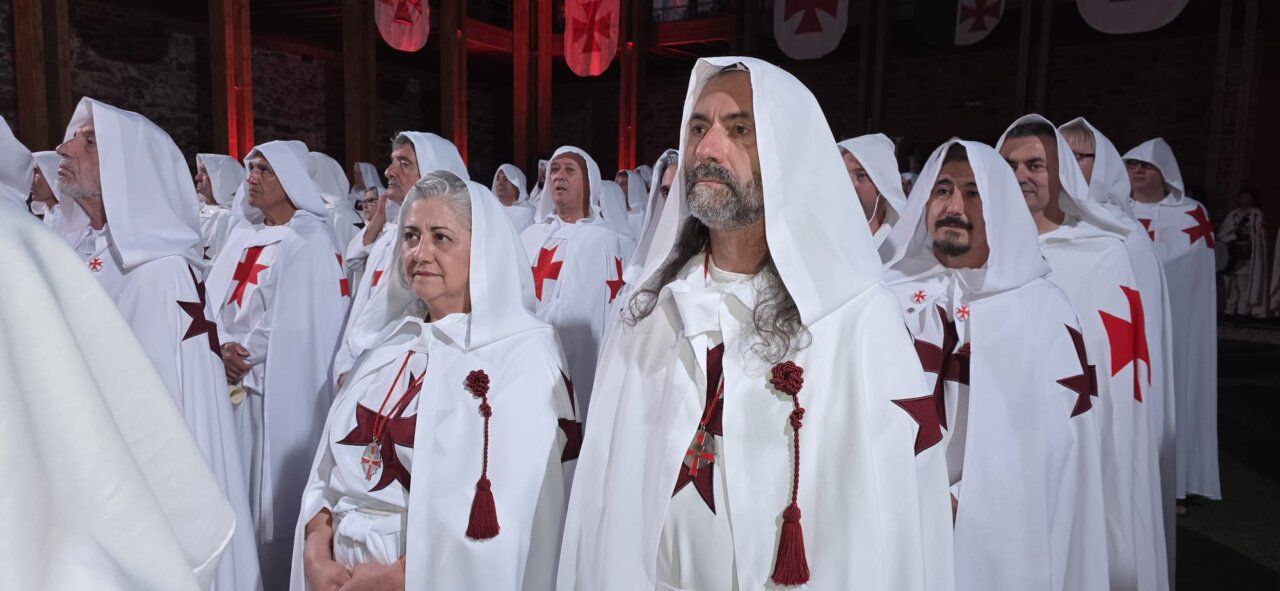 Ceremonia de ordenación templaria con participantes en túnicas blancas y cruces rojas.
