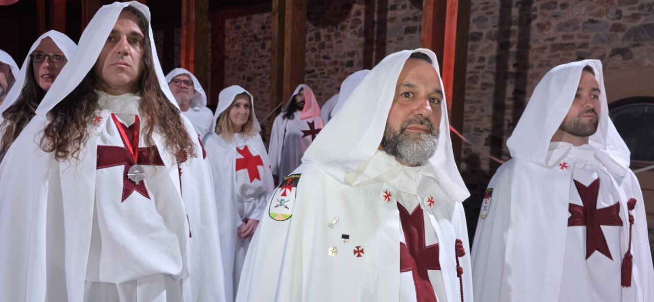 Grupo de personas en ceremonia de ordenación templaria con capas blancas y cruces rojas