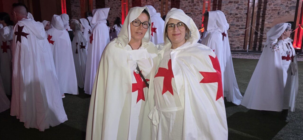 Dos mujeres vestidas con capas blancas y cruces rojas en un evento