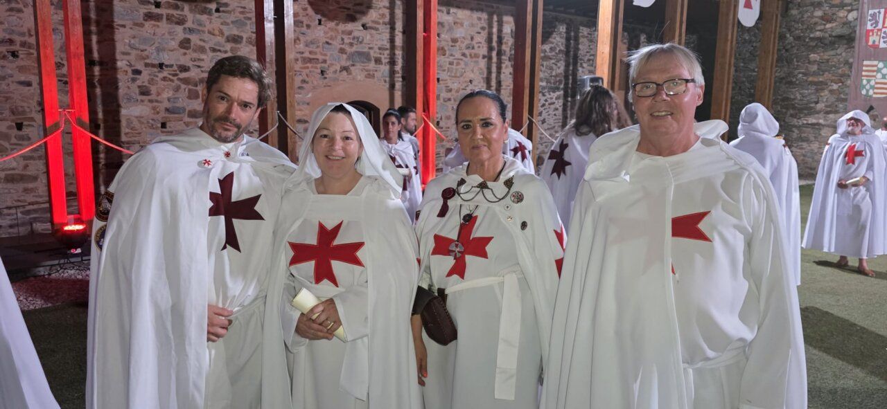 Cuatro personas vestidas con túnicas blancas y cruces rojas en un evento templario.