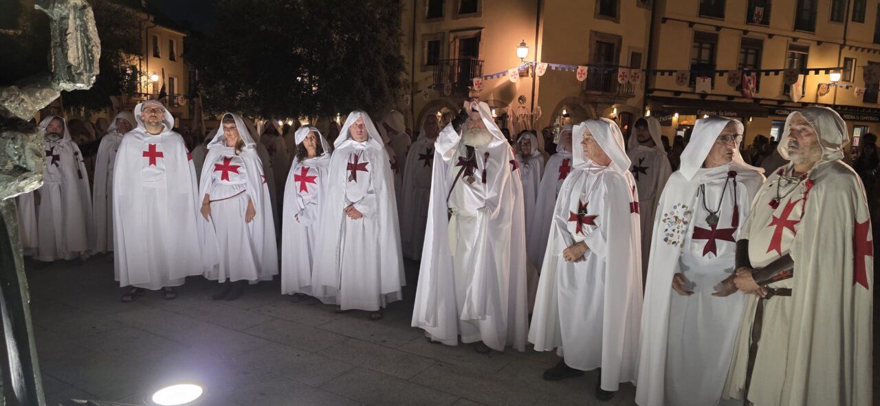Grupo de personas vestidas con túnicas blancas y cruces rojas en una ceremonia nocturna.