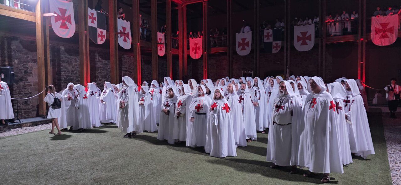 Ceremonia de ordenación templaria con participantes en túnicas blancas y cruces rojas