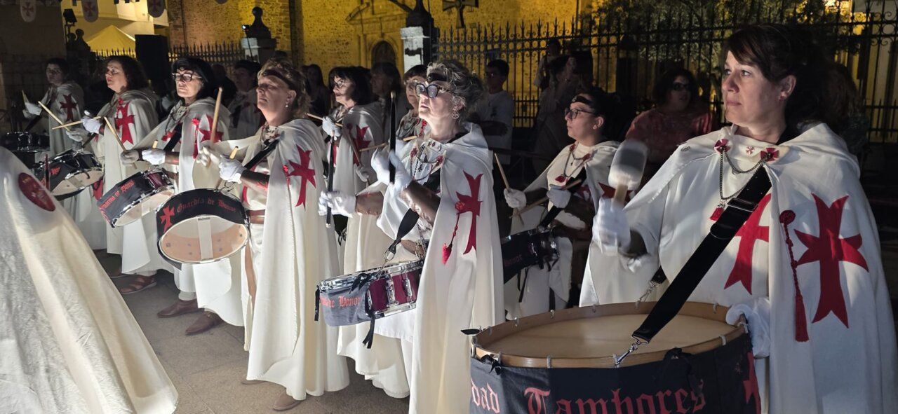 Mujeres con capas blancas y cruces rojas tocando tambores en un evento